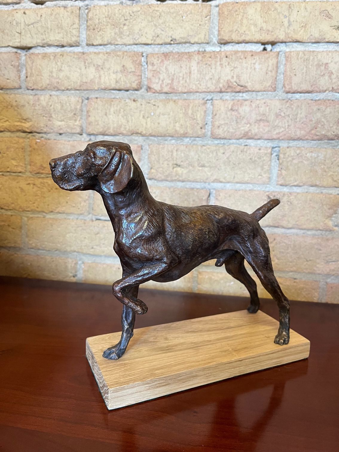 A bronze statue of a dog is standing on its hind legs on a wooden base.
