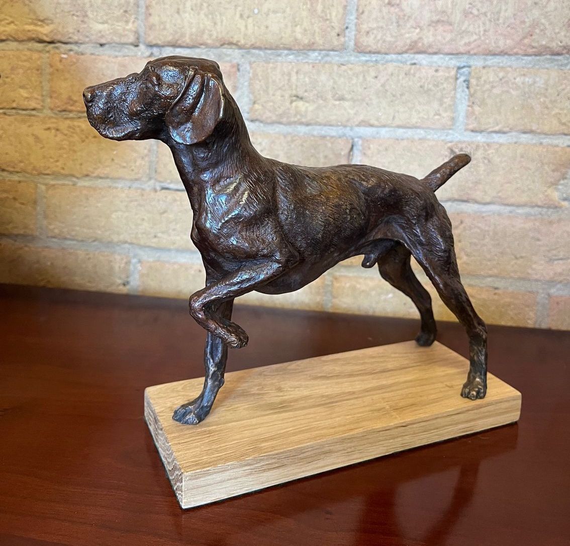 A bronze statue of a dog is standing on a wooden base on a table.