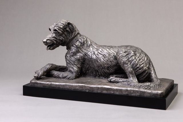 A statue of a dog laying down on a black base.
