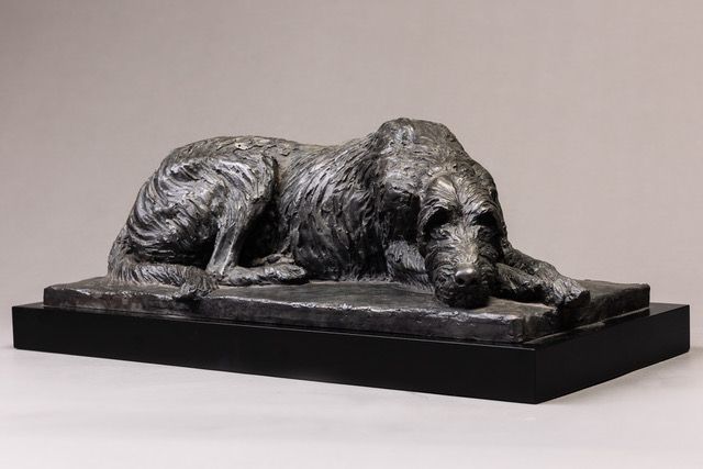 A statue of a dog laying down on a black base.