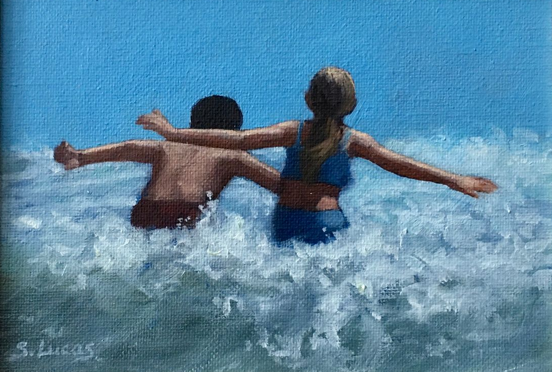 Two people with arms outstretched wade into the ocean, water splashing around them against a bright blue sky.