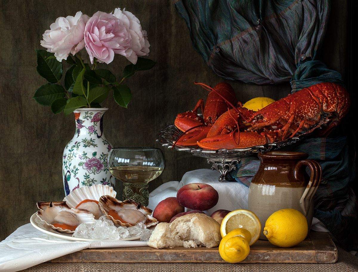 Still life: Lobster, shellfish, lemons, bread, flowers, and wine on a table.
