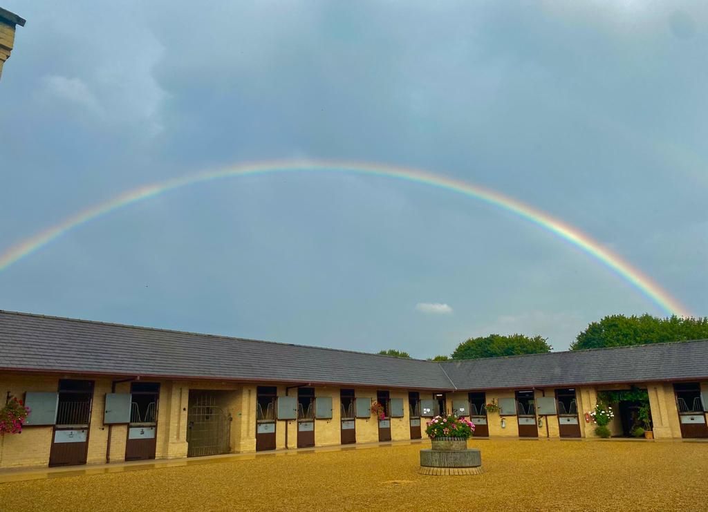 A rainbow is visible over a row of horse stables