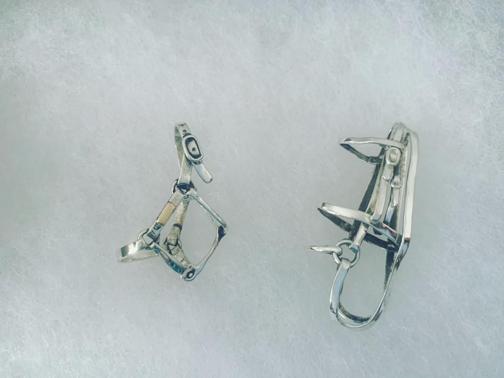 Silver-toned metal horse bridle, seen from a side view. It is set on a light brown woven mat.