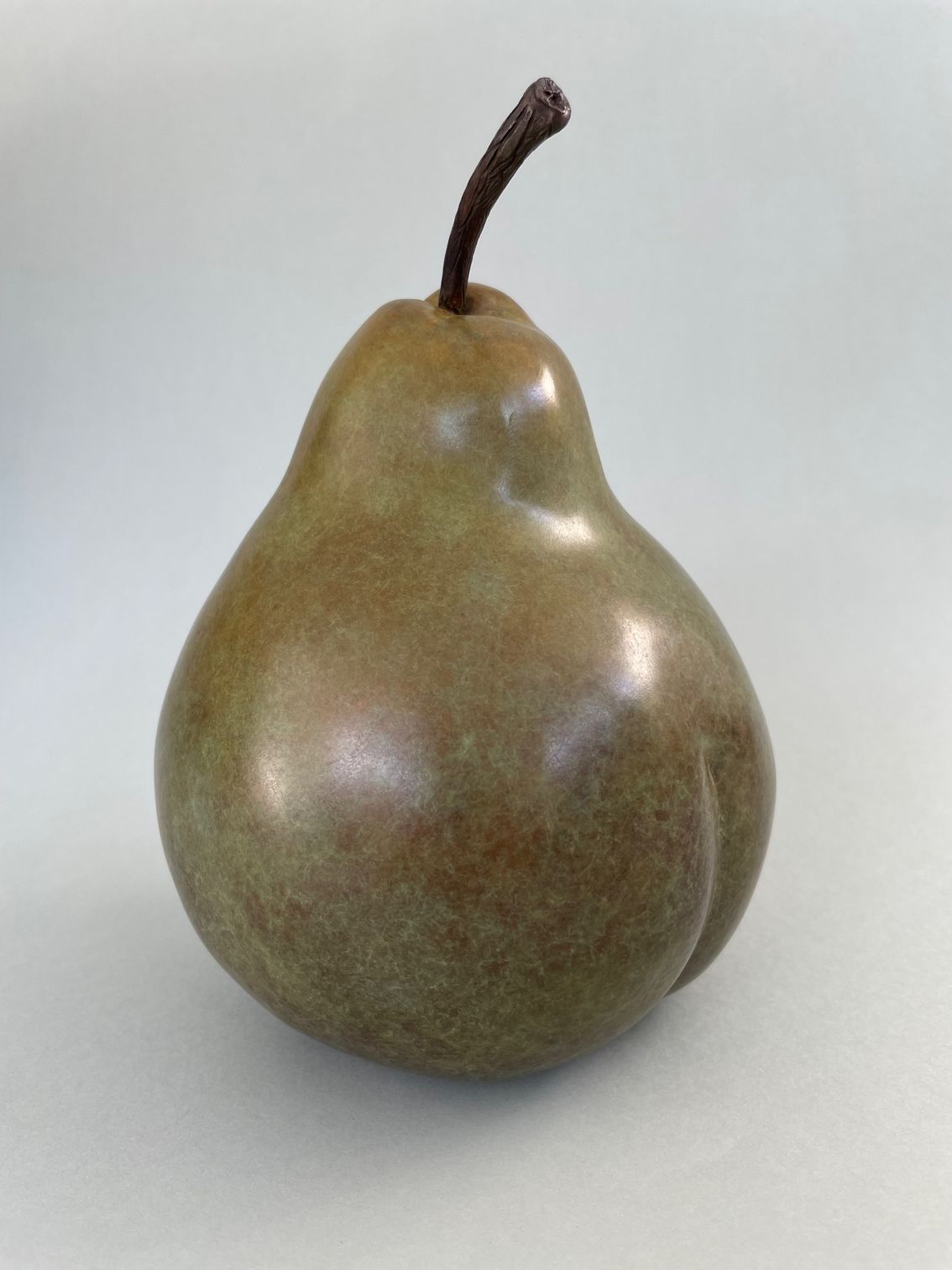 Green and brown pear with dark stem, on a gray background.