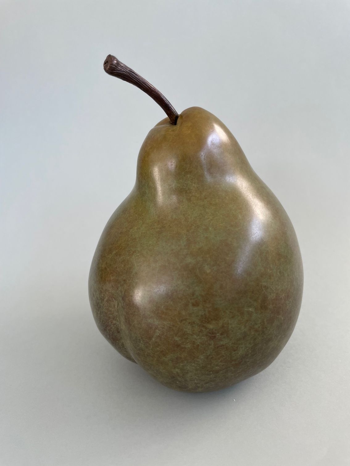 A bronze pear with a brown stem is sitting on a white surface.