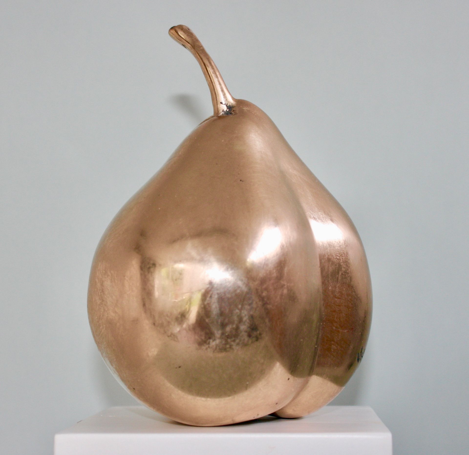 A copper sculpture of a pear is sitting on a white pedestal