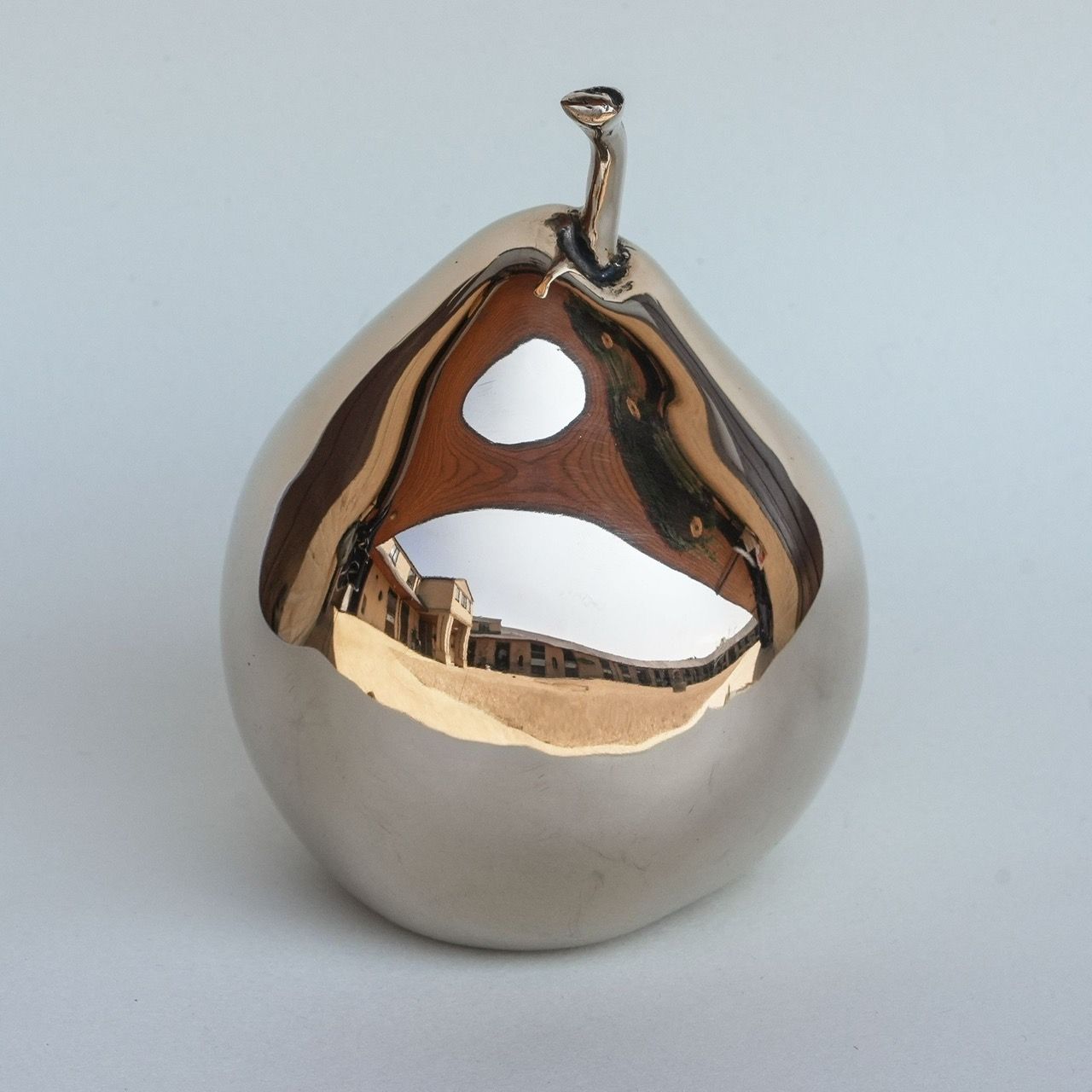 A silver pear with a reflection of a building in it