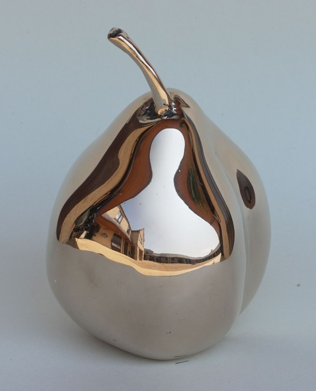 A silver pear with a gold stem sits on a white surface