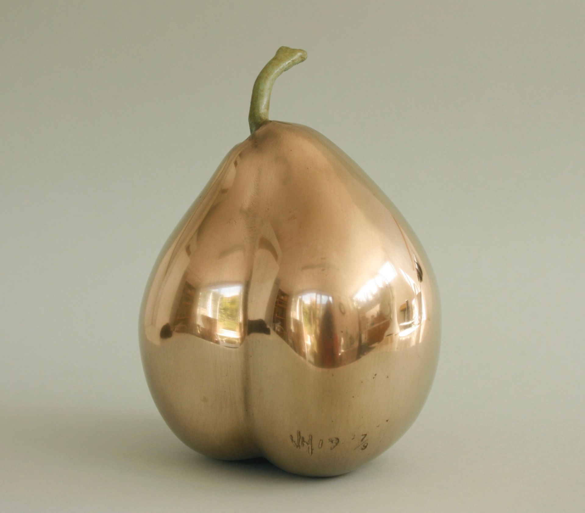 Shiny, copper-colored pear sculpture with a green stem, reflecting light.
