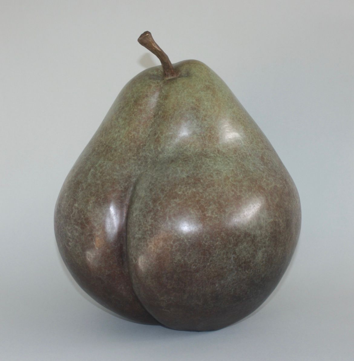 A green pear with a brown stem on a white surface