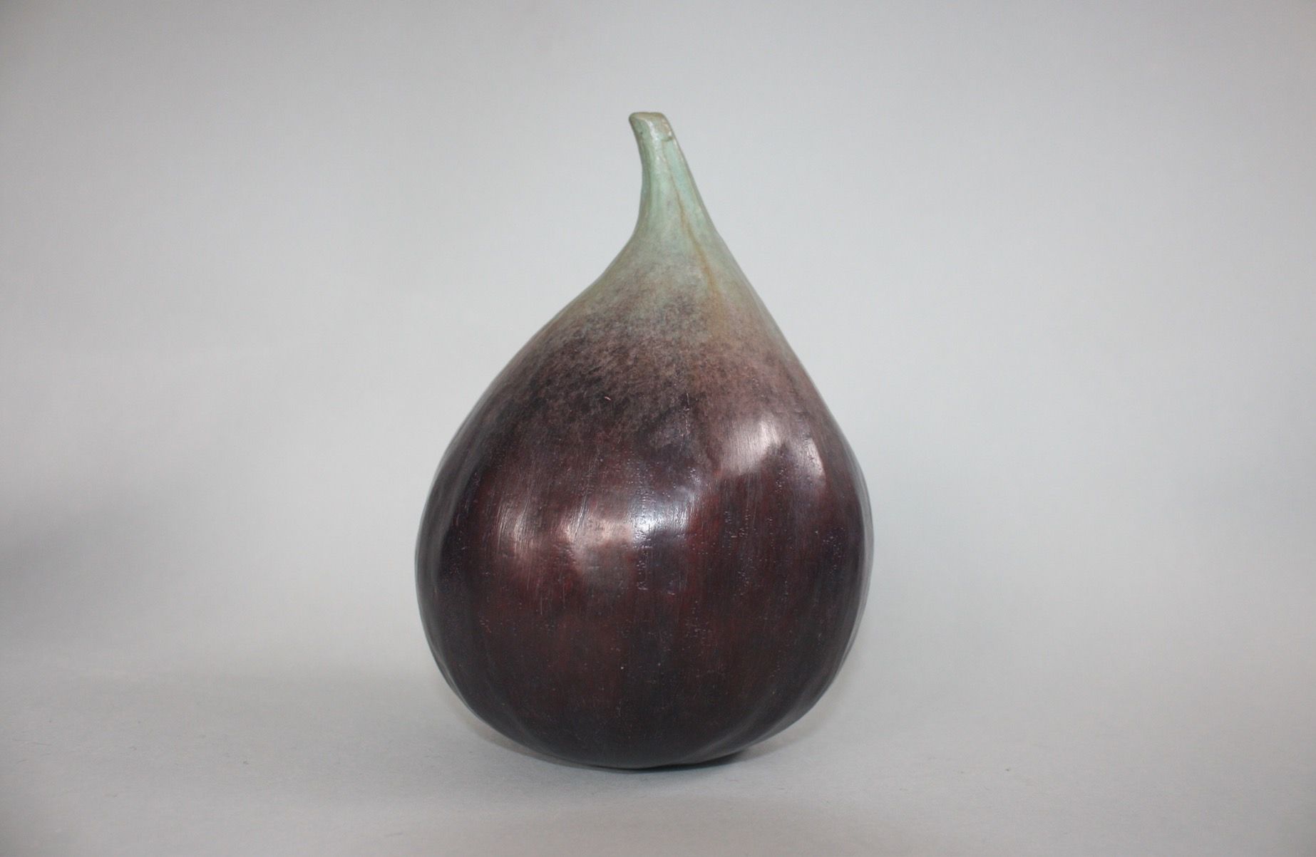 A purple fig with a green stem is sitting on a white surface.