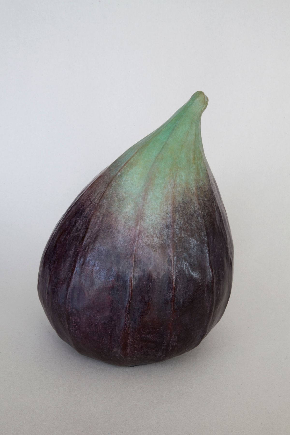 A bronze purple fig with a green stem is sitting on a white surface.