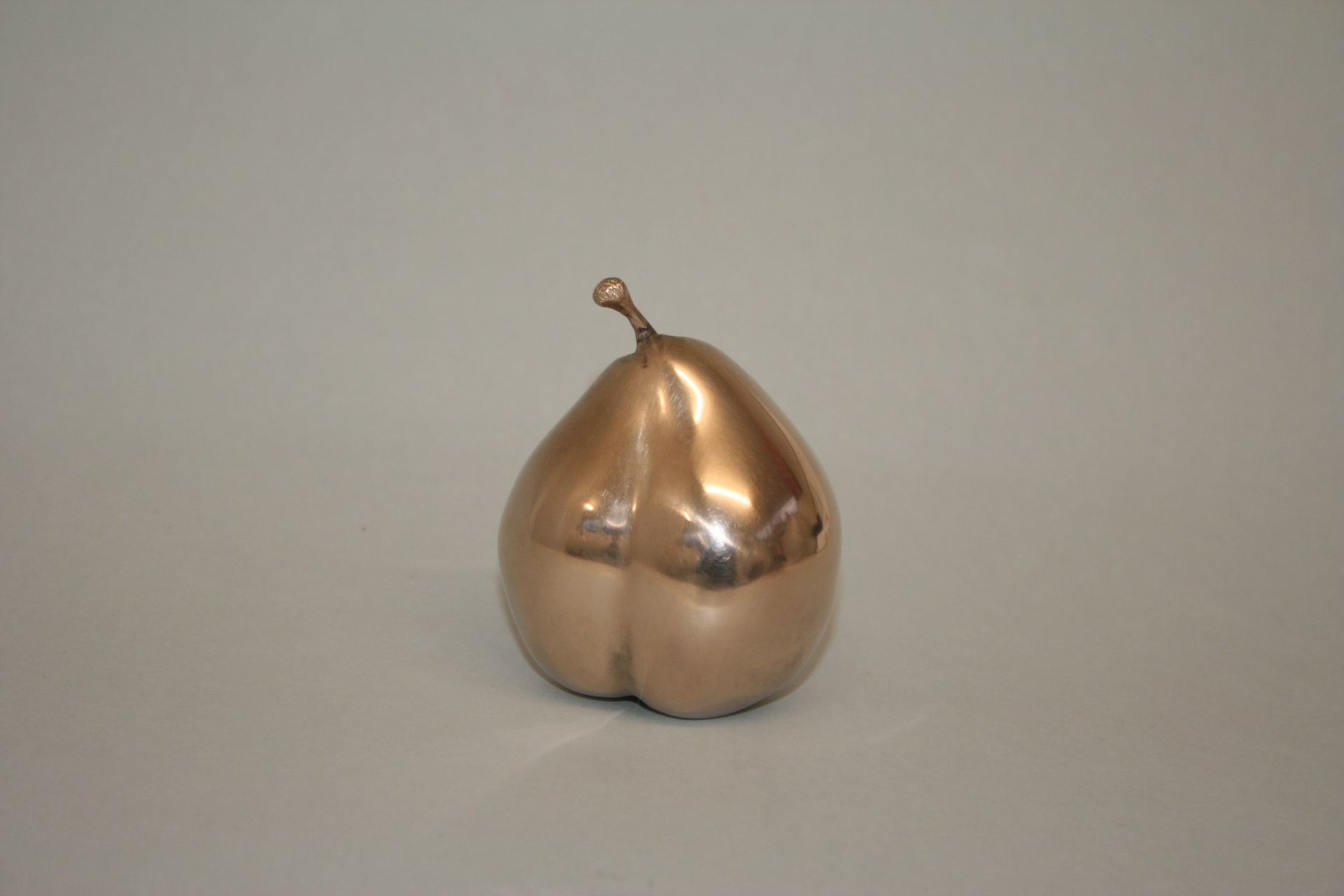 A bronze pear is sitting on a white surface.