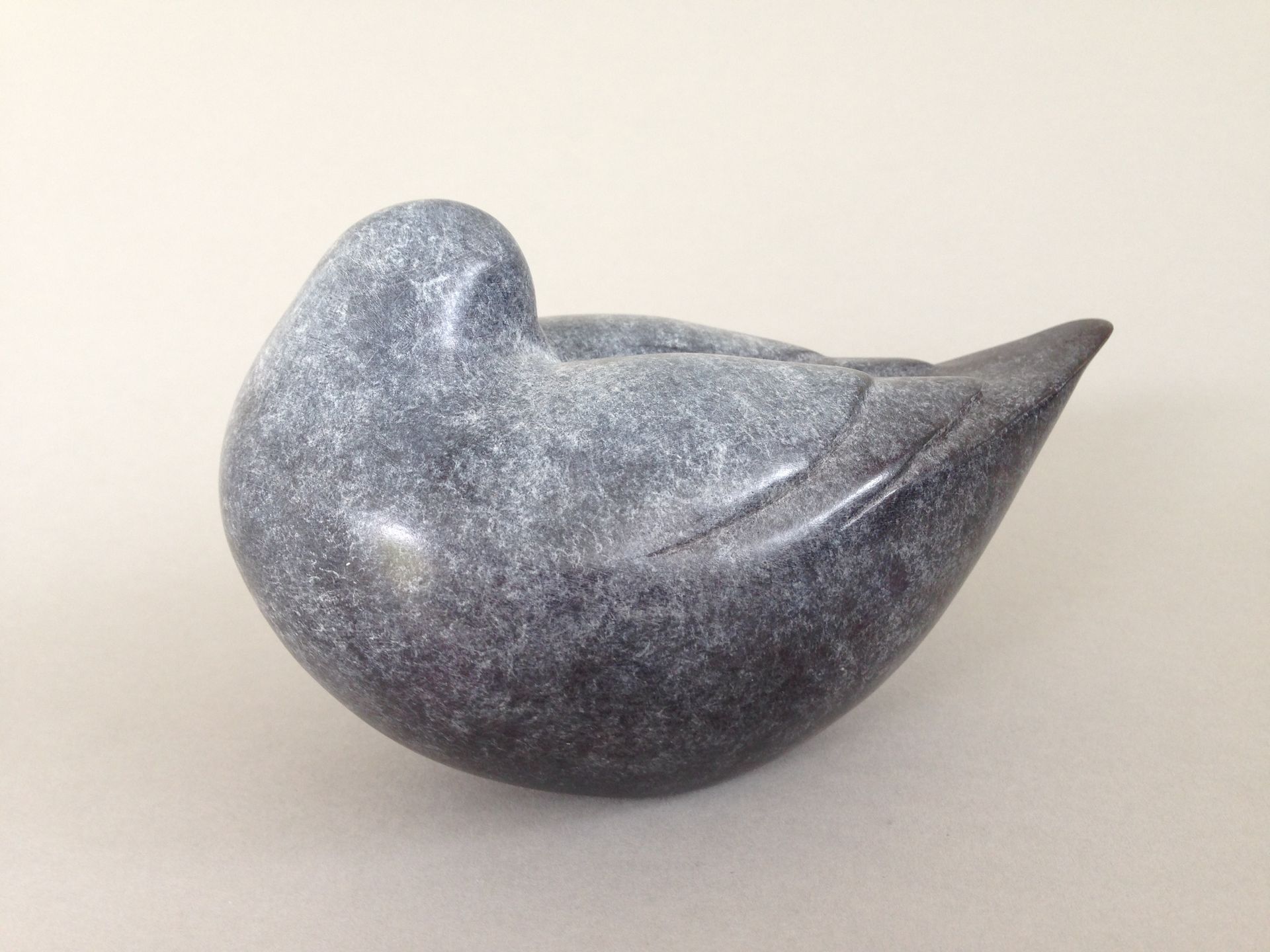 A small statue of a bird is sitting on a white surface.