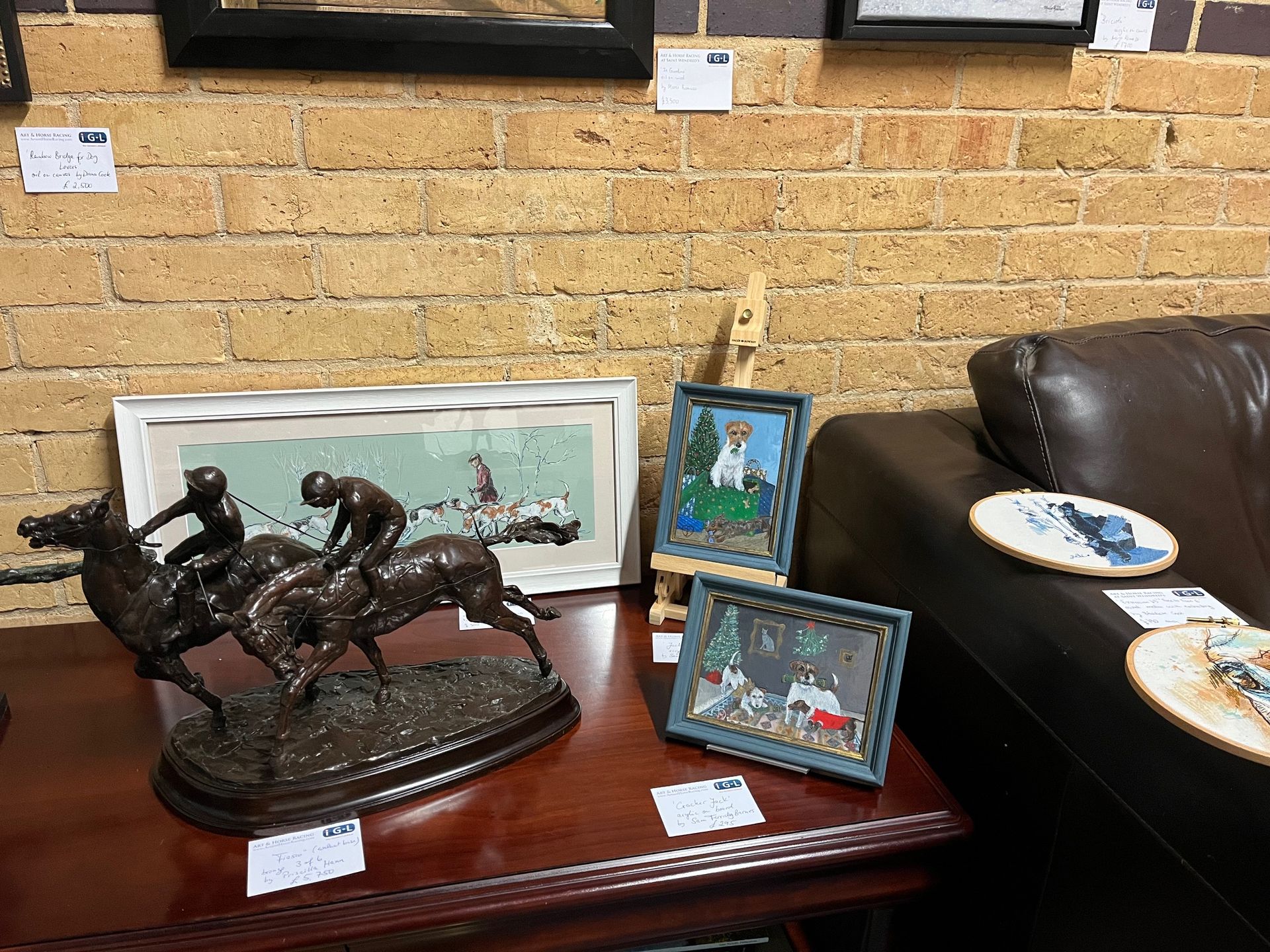 Bronze horse racing statue, paintings, and framed artwork on a table in front of a brick wall.
