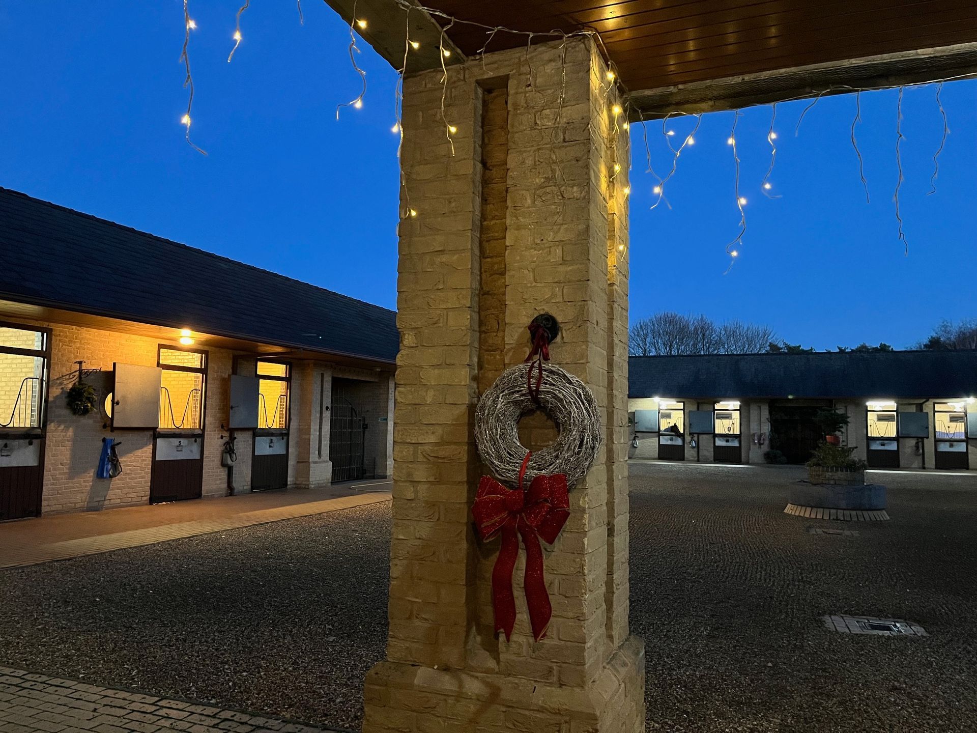Stable courtyard at dusk decorated with Christmas lights and a wreath.