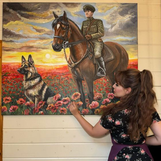 A woman is painting a painting of a man riding a horse in a field of poppies.