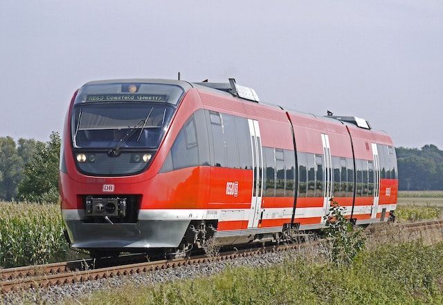 Red and white passenger train traveling on tracks through a field.