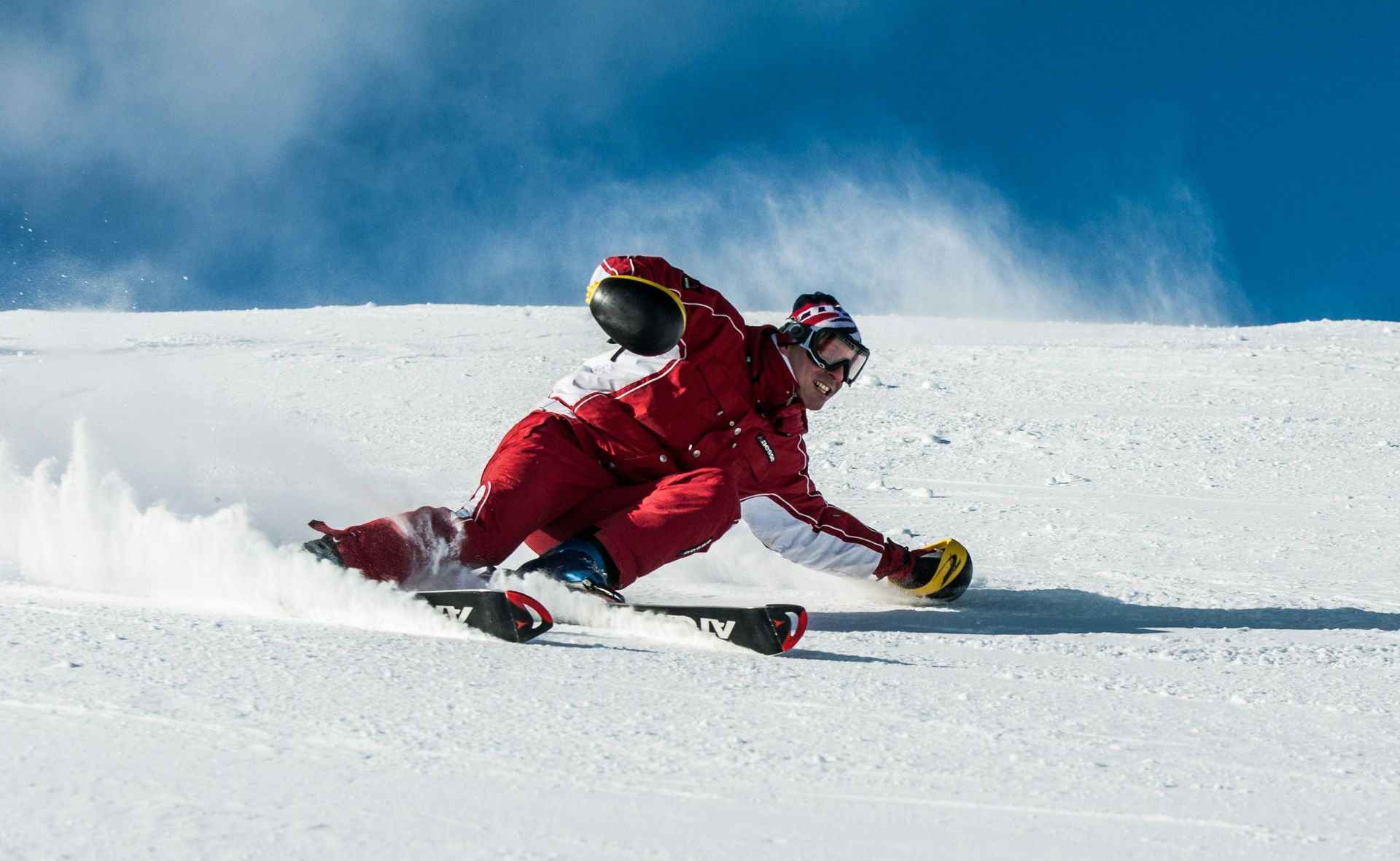 Skier in red racing suit carving turns in the snow. Blue sky overhead.