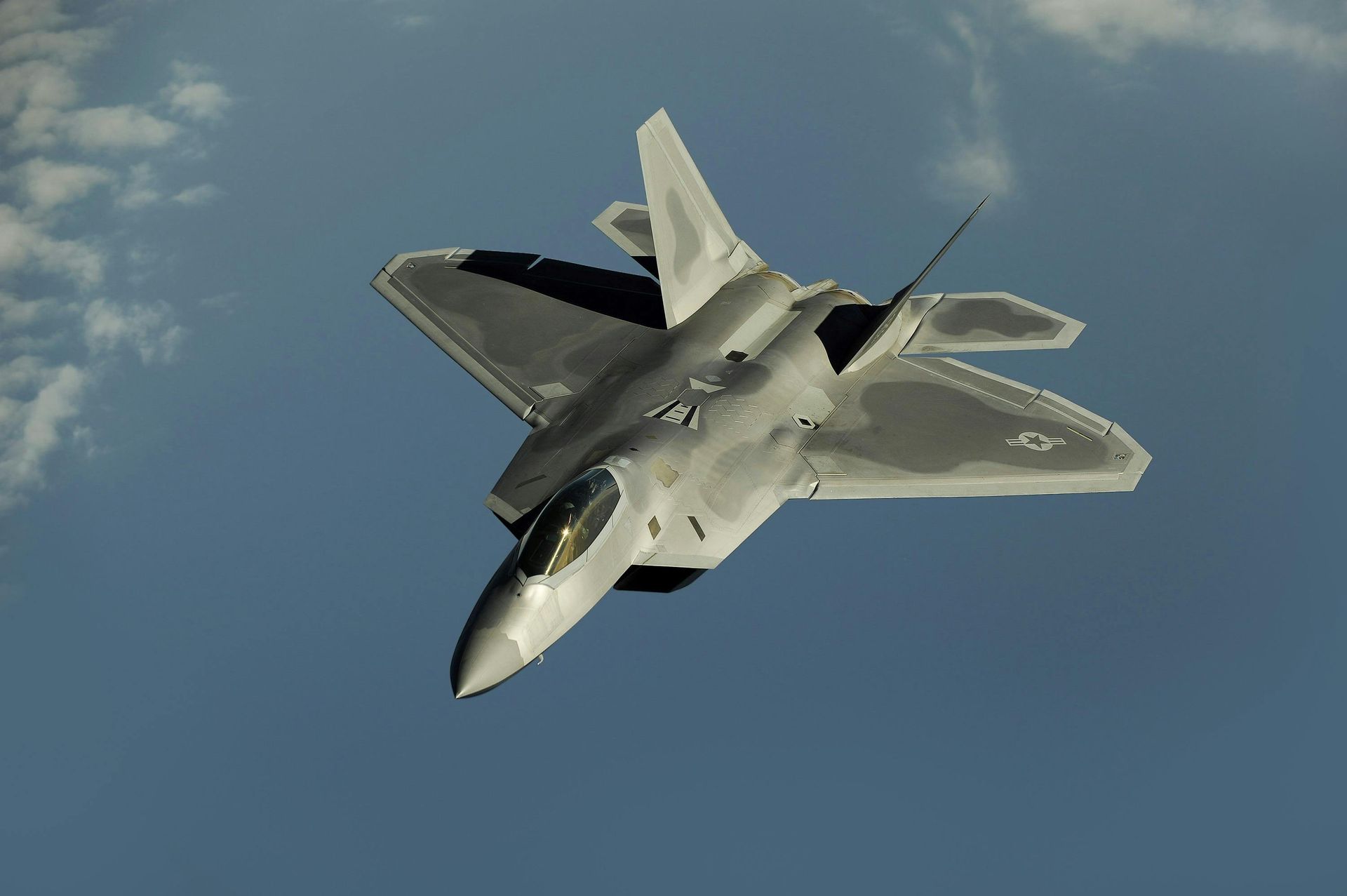 F-22 Raptor fighter jet in flight against a blue sky, angled upwards.