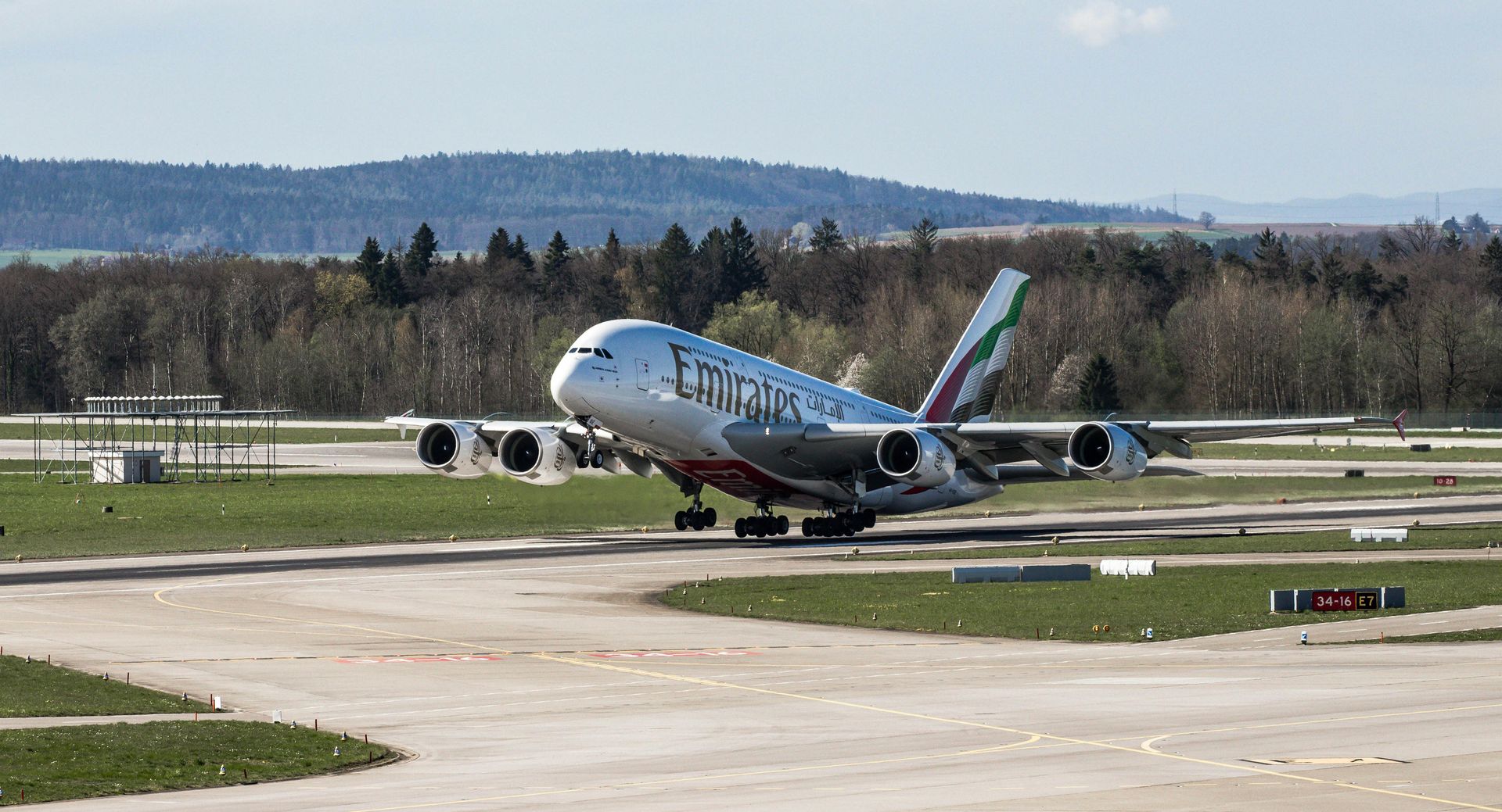 An Emirates A380 airplane takes off from a runway with a green and brown landscape in the background.