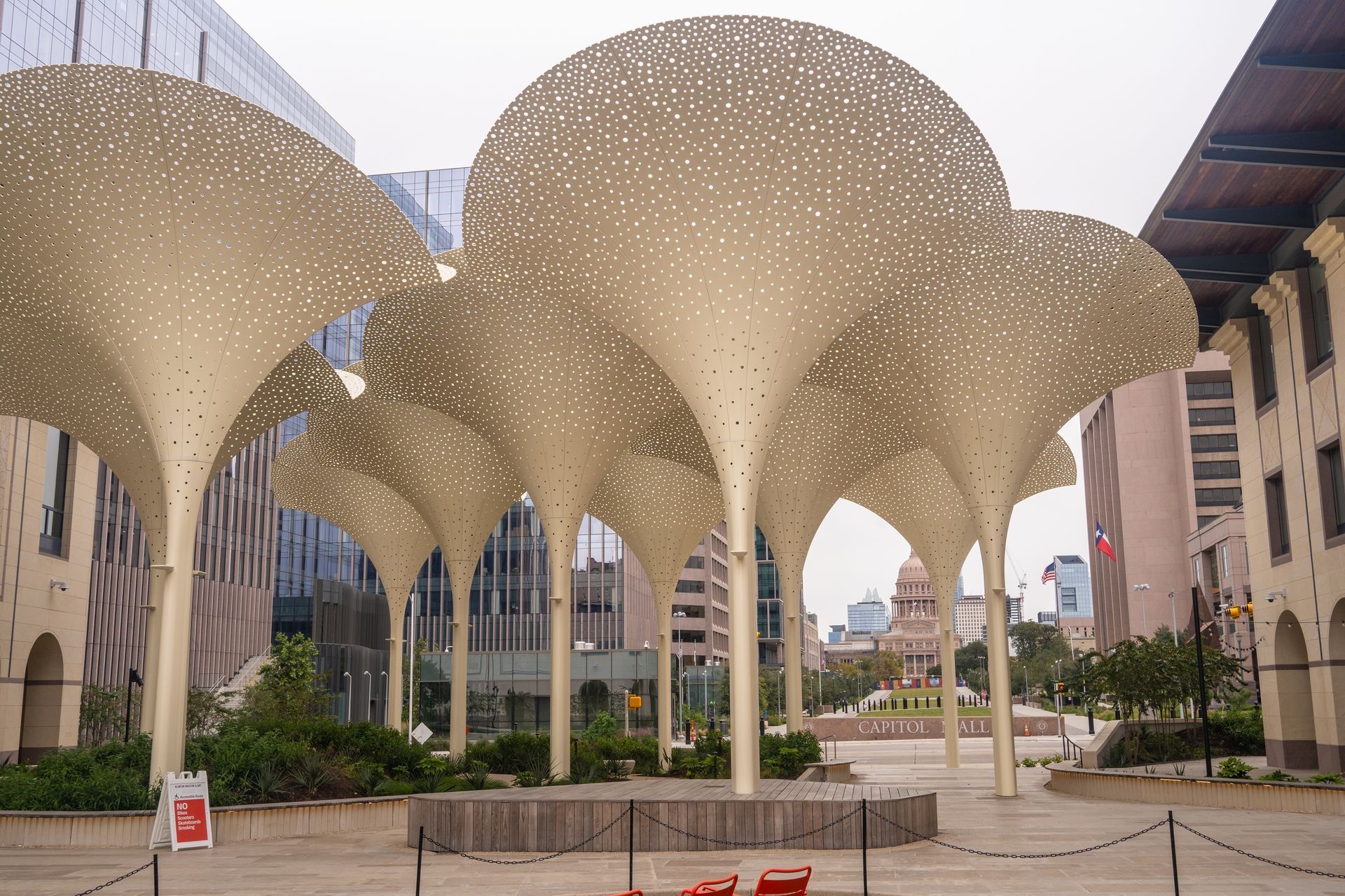 Modern art installation of gold-colored, tree-like structures in a plaza, with buildings and Capitol in the background.