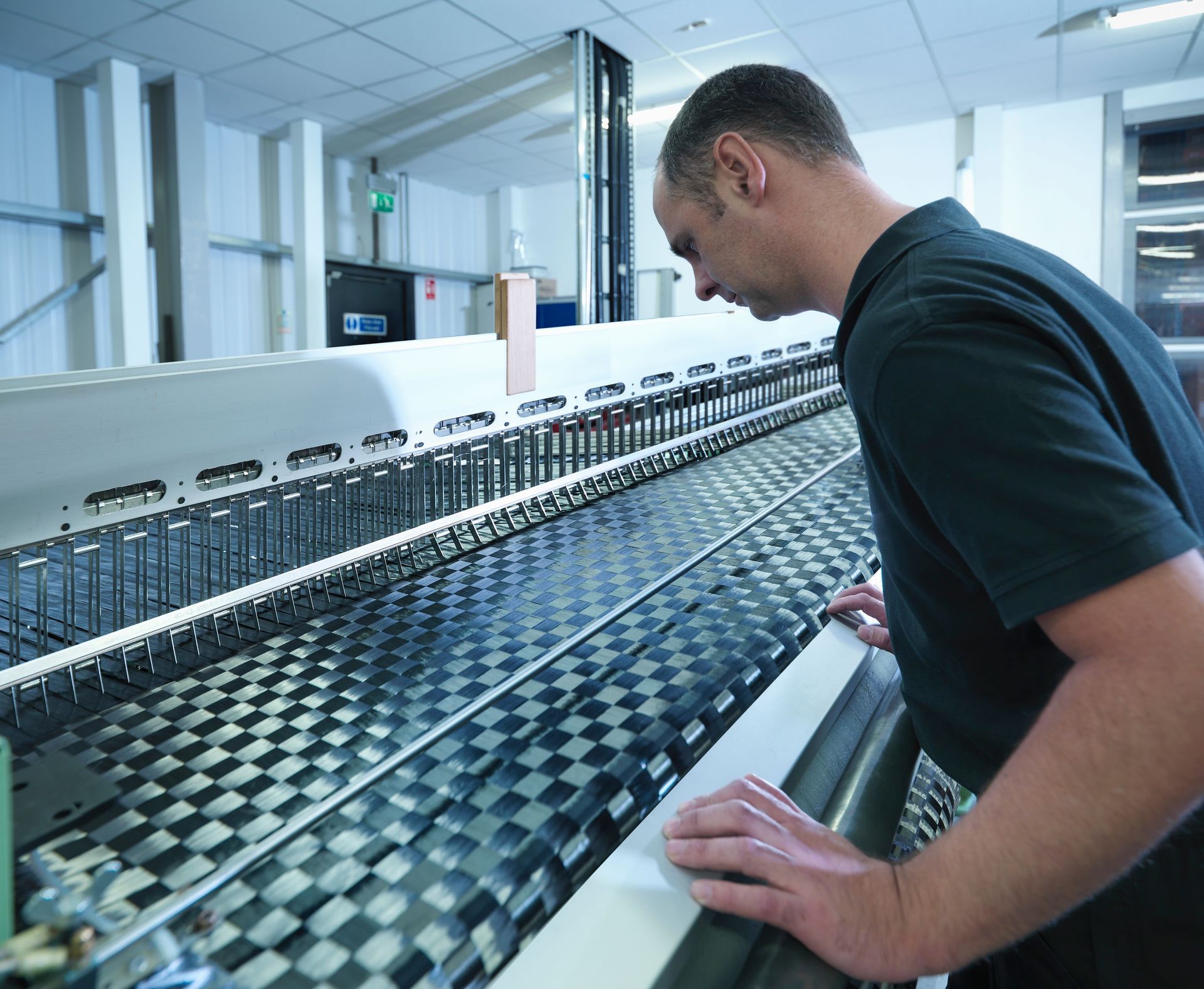 Man inspects a black and white checkered fabric on a large industrial machine in a factory setting.