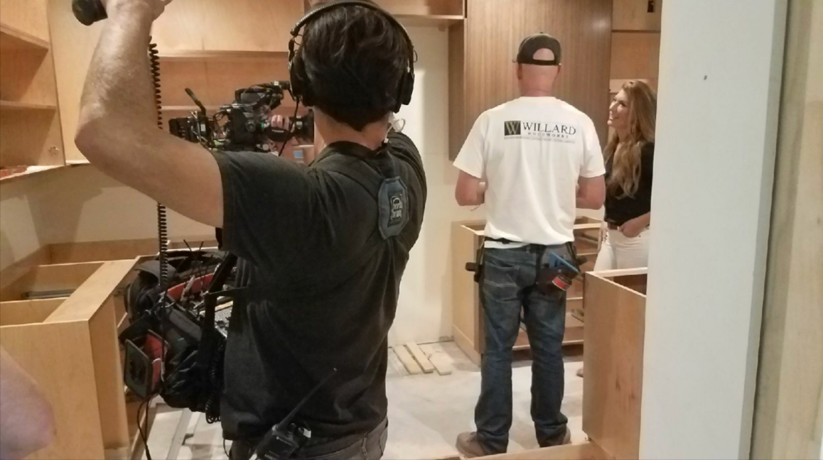 People unloading boxes in a room, with one person lifting items from a pile and another standing nearby.