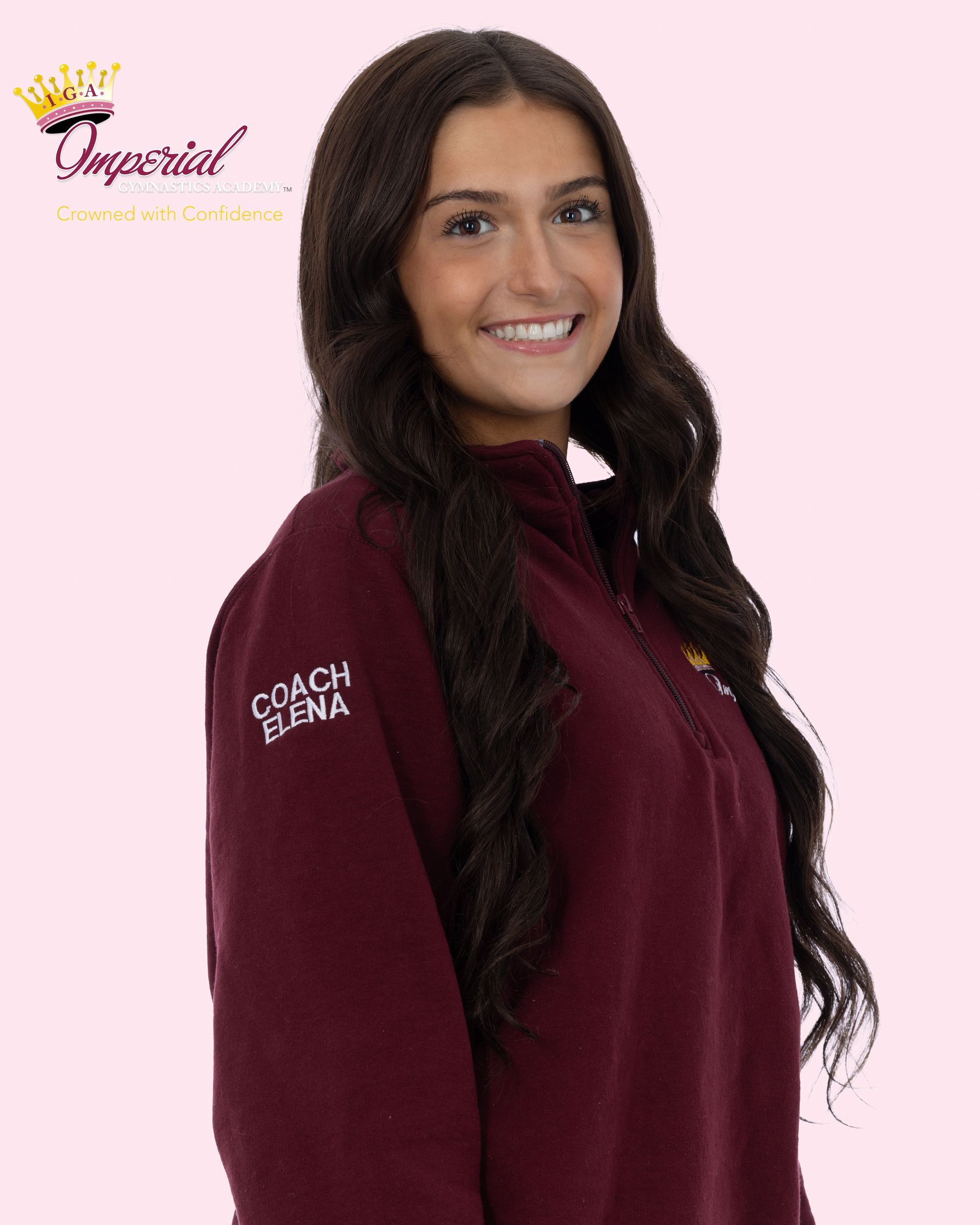 Woman with long, wavy brown hair smiles at the camera, wearing a plaid shirt and necklaces; outdoors.