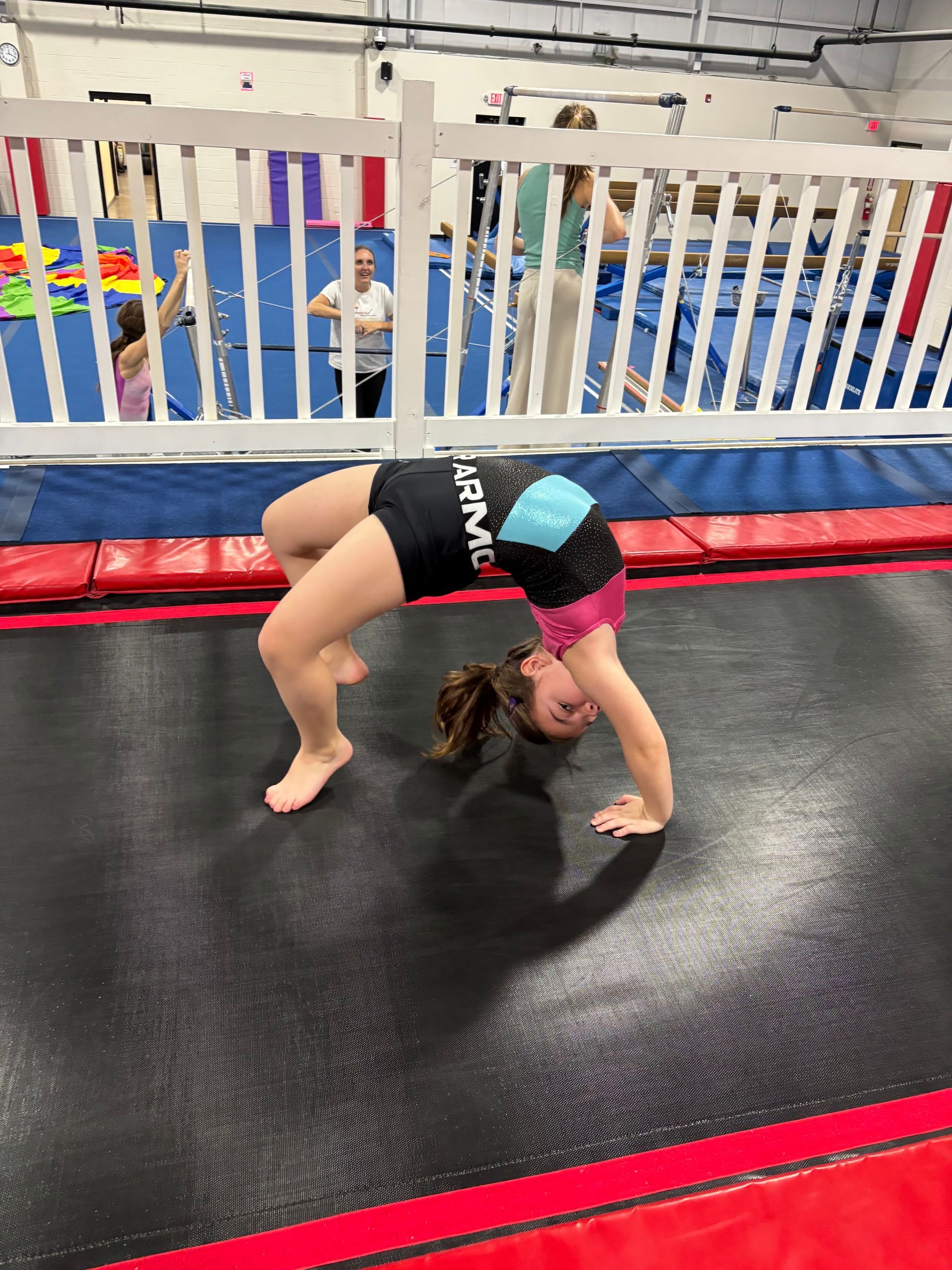 Girl in athletic wear doing a backbend on a trampoline in a gym.