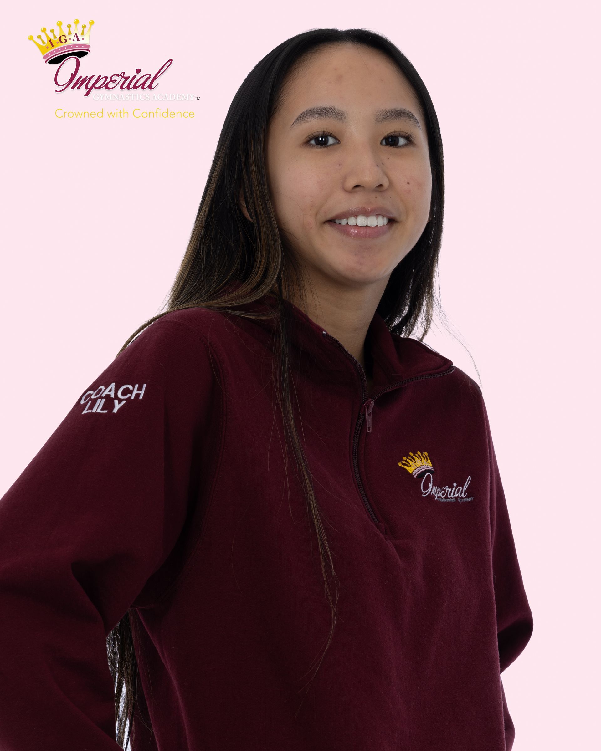 Woman with long dark hair, wearing a pink collared shirt and gold necklace, smiling at the camera.