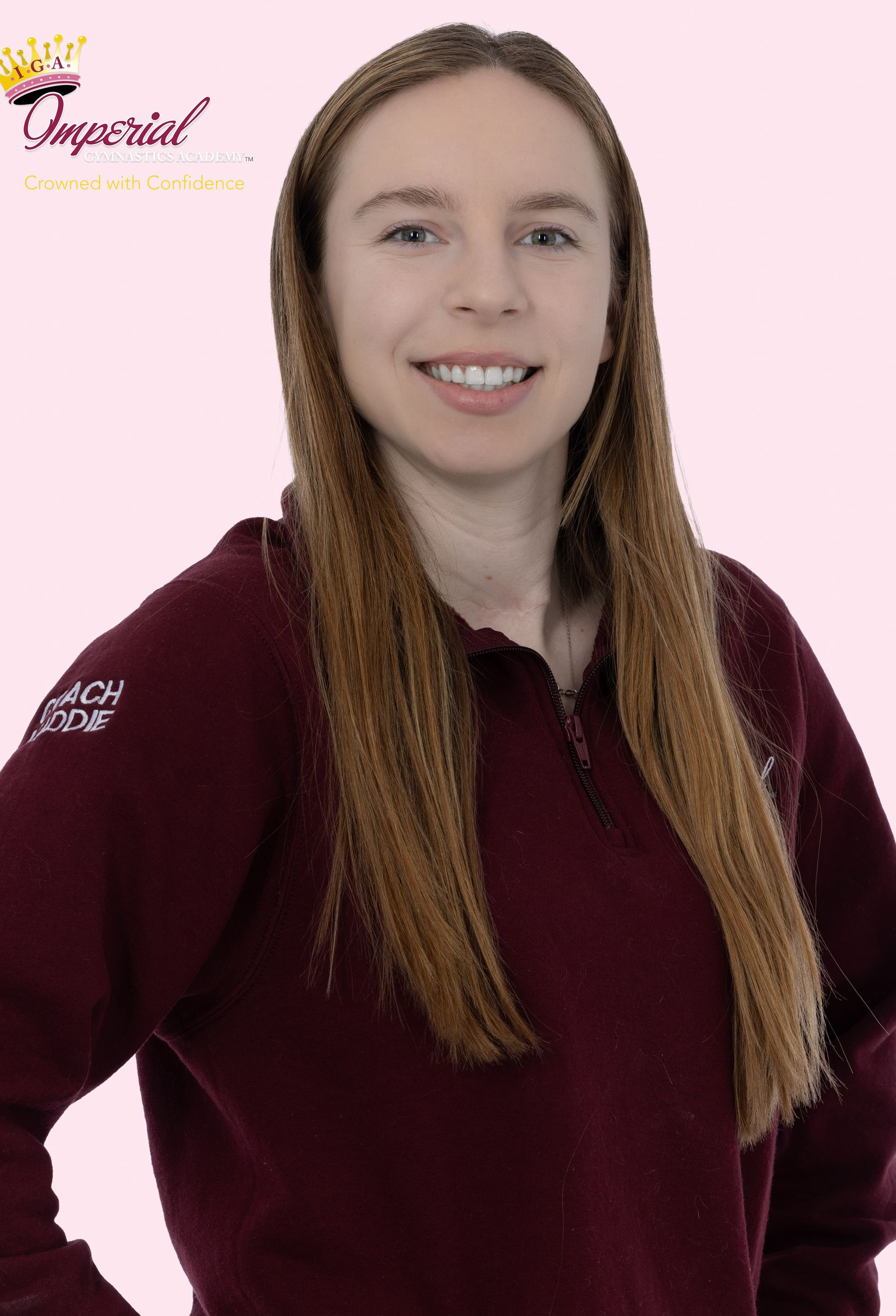 Woman with long brown hair, smiling, wearing a maroon t-shirt with 
