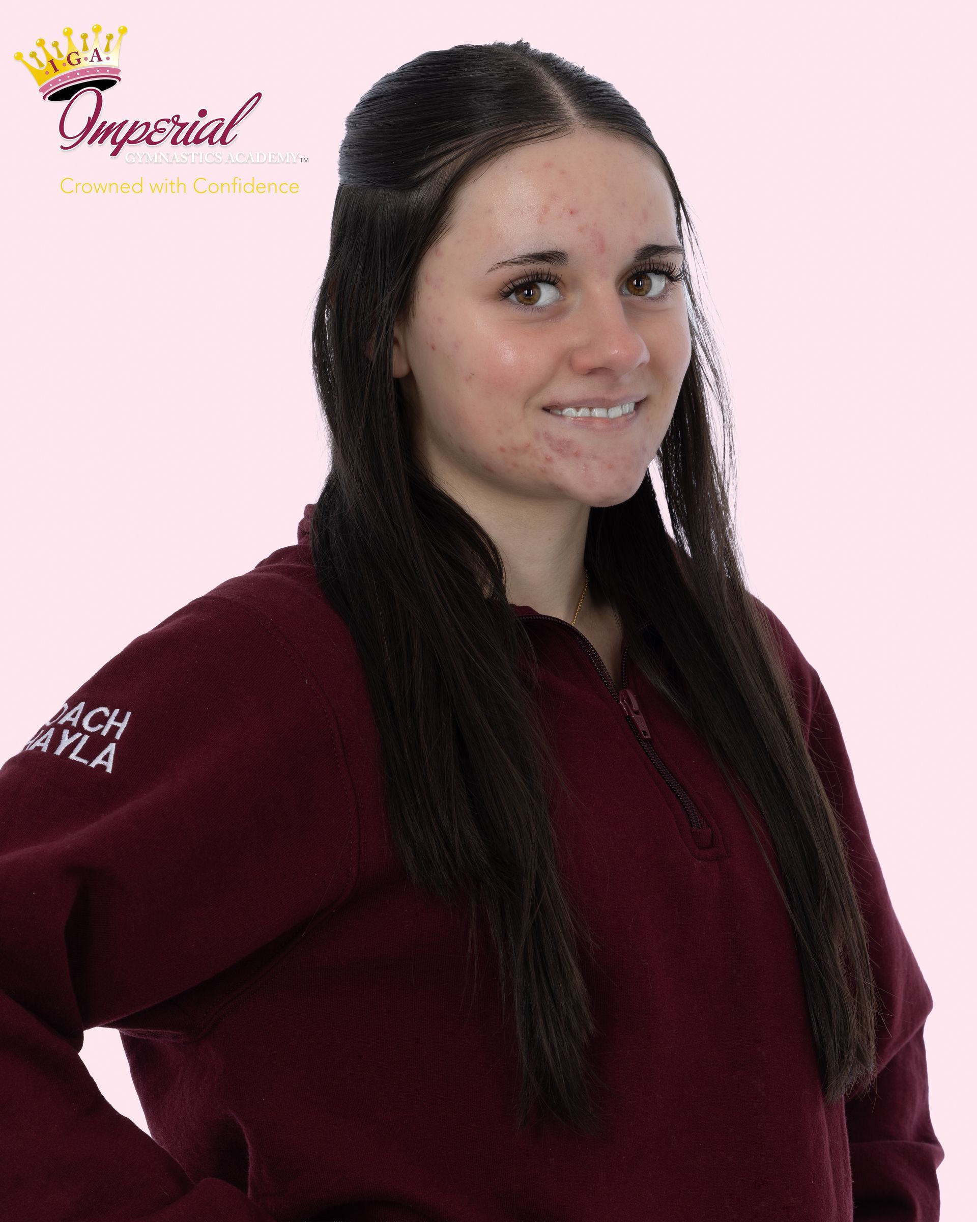 A young person with dark wavy hair smiles outdoors, wearing a black shirt.