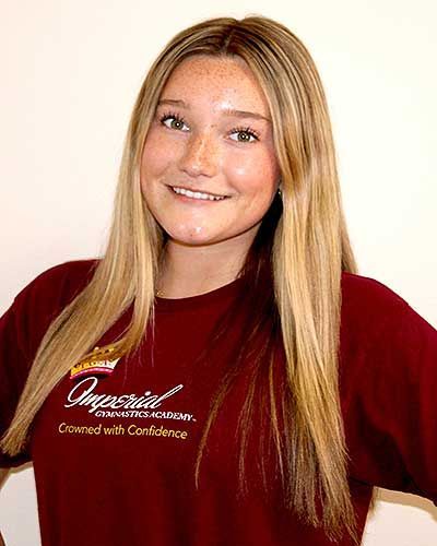 Blonde-haired person smiling, wearing a maroon shirt with