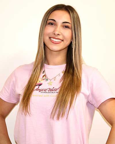 Woman with long blonde hair, smiling, wearing a pink t-shirt and necklace.