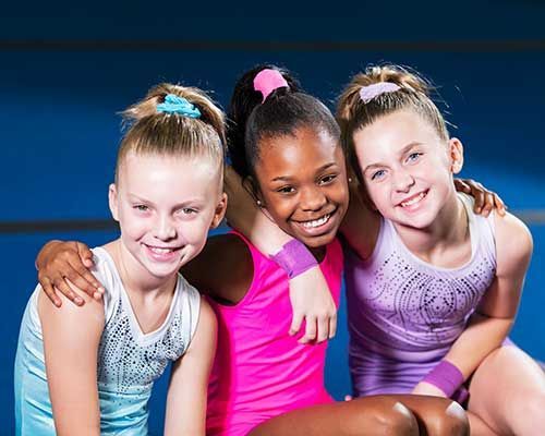 Three smiling girls in athletic wear, arms around each other.