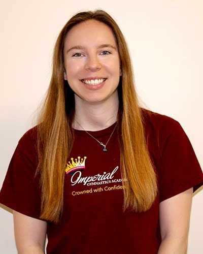 Woman with long brown hair, smiling, wearing a maroon t-shirt with