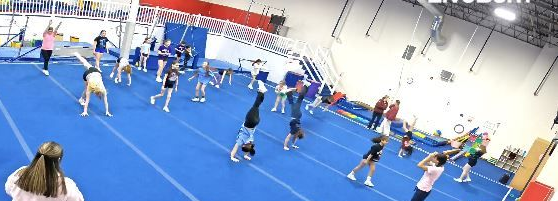 Cheerleaders in pink and black outfits running and practicing in a gym on blue mats.