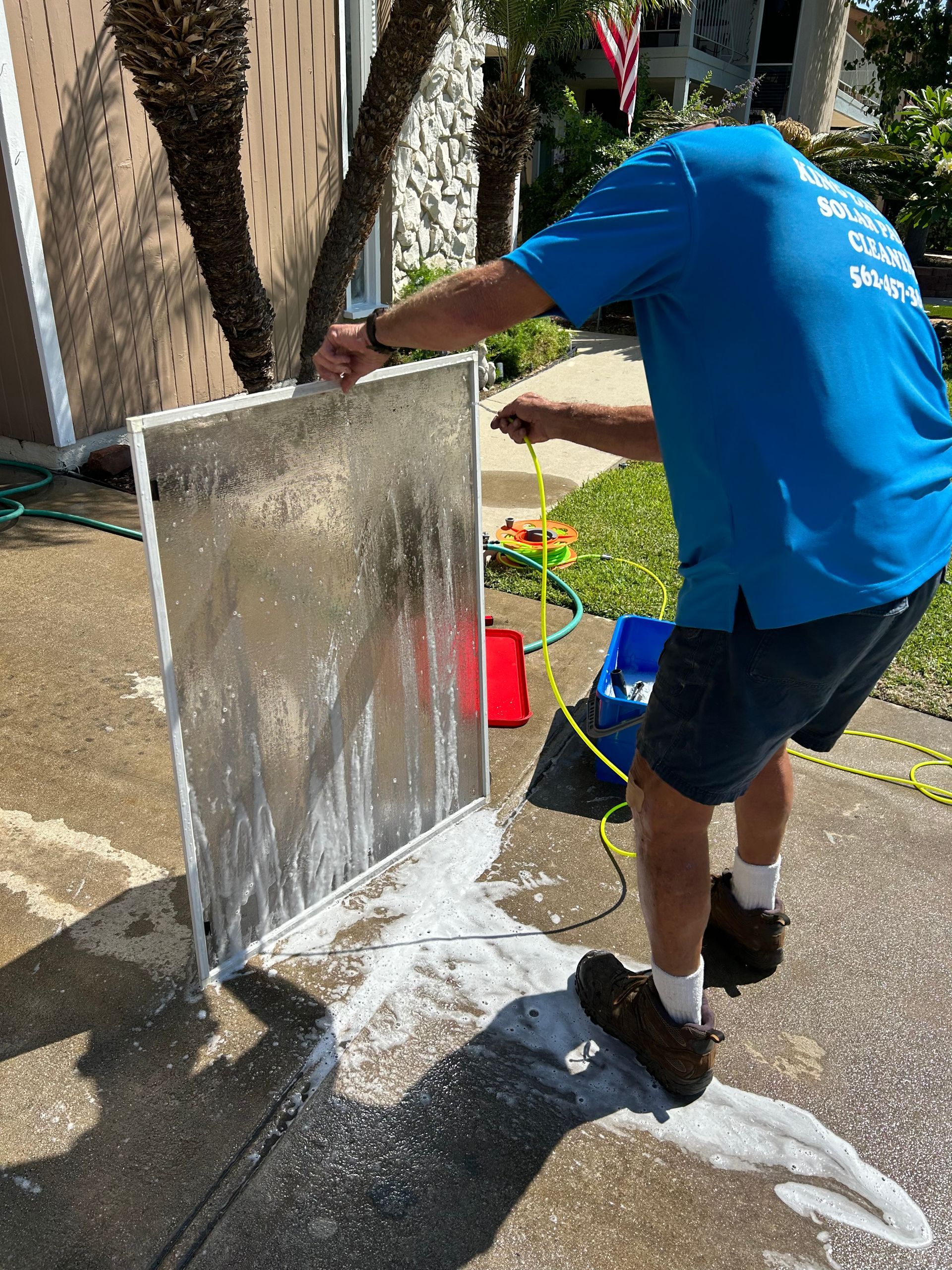A man in a blue shirt is cleaning a screen door with a hose.