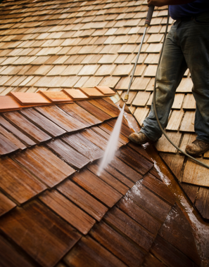 A man is cleaning a wooden roof with a high pressure washer