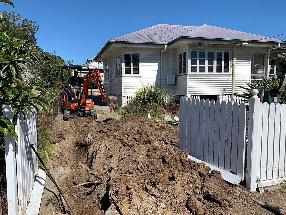 A Small Excavator is Digging a Hole in Front of a House — Beards Roofing and Plumbing in Burpengary, QLD