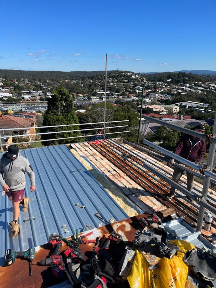 A Man is Standing on Top of a Metal Roof — Beards Roofing and Plumbing in Sunshine Coast, QLD