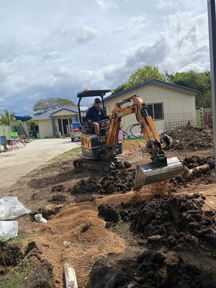 A Man is Driving a Small Excavator on a Dirt Road — Beards Roofing and Plumbing in North Lakes, QLD