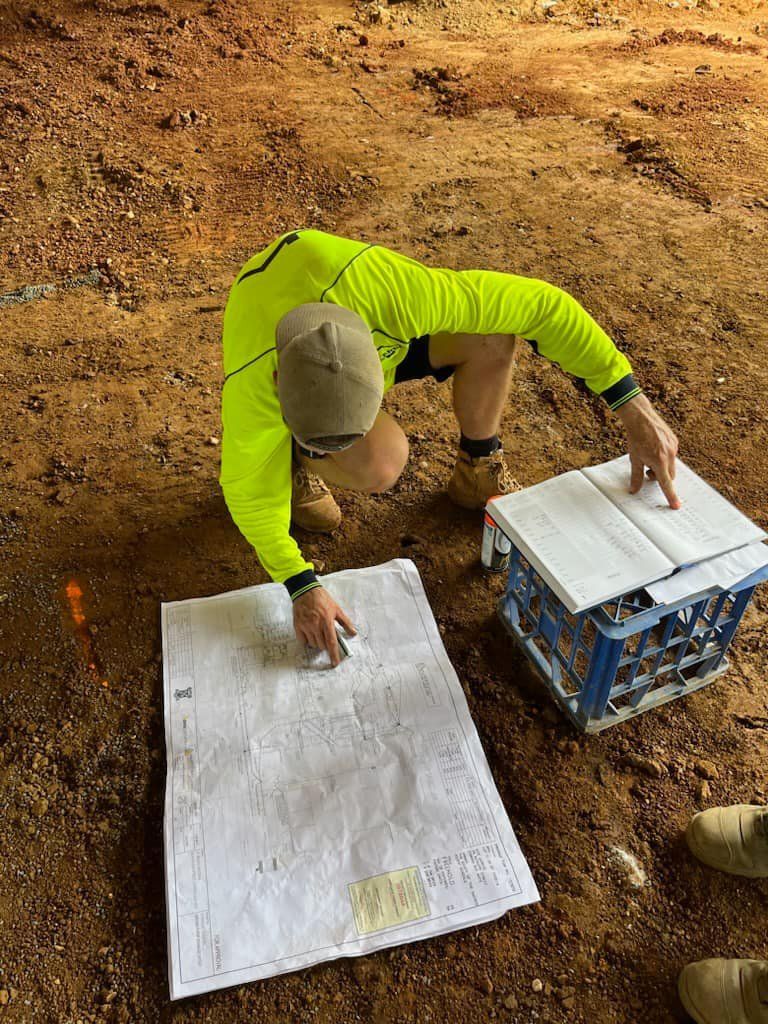 A Man is Kneeling Down on the Ground Looking at a Map — Beards Roofing and Plumbing in Bribie Island, QLD
