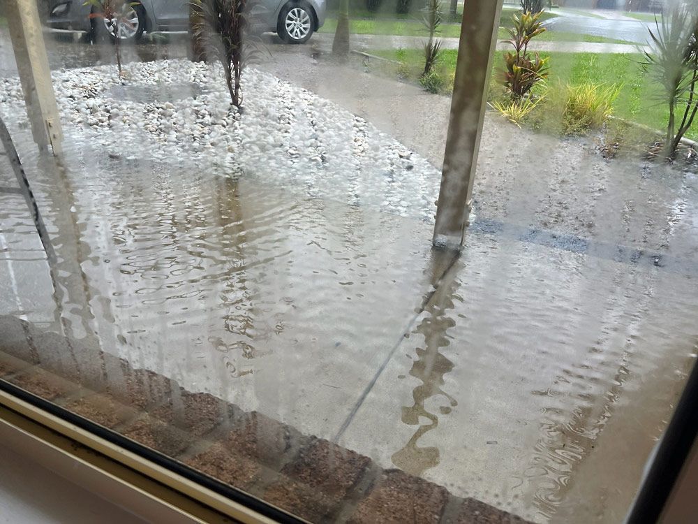 A Window Shows a Flooded Driveway With a Car Parked in the Background — Beards Roofing and Plumbing in Sunshine Coast, QLD