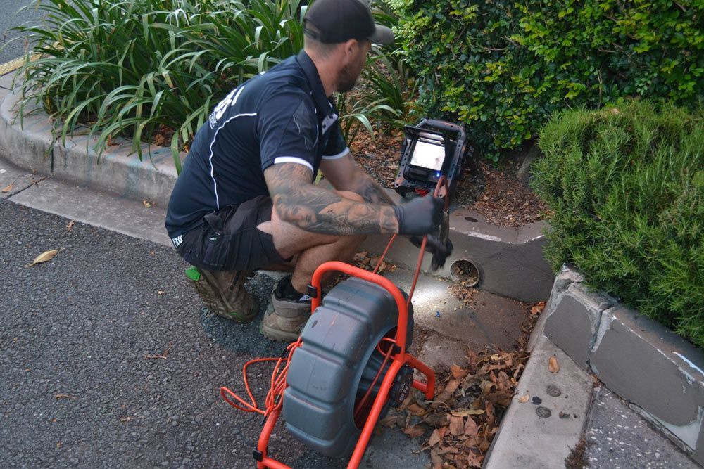A Man is Kneeling Down on the Side of the Road Using a Camera — Beards Roofing and Plumbing in Morayfield, QLD