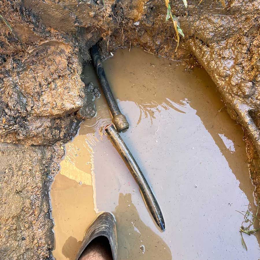 A Person is Standing in a Muddy Puddle Next to a Pipe — Beards Roofing and Plumbing in Caboolture, QLD