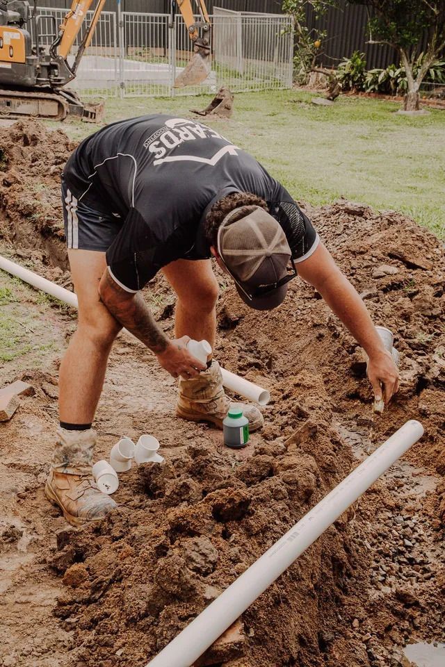 Man is Working on a Pipe in the Dirt — Beards Roofing and Plumbing in Clontarf, QLD