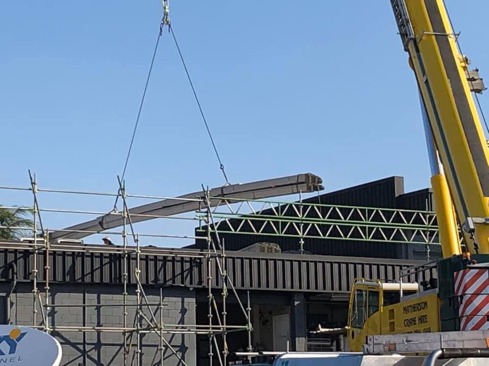 A Large Yellow Crane is Lifting a Large Piece of Metal — Beards Roofing and Plumbing in Kallangur, QLD